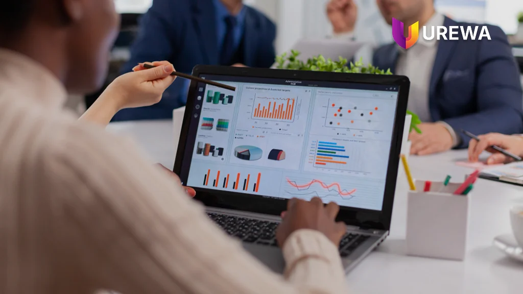 A management team reviewing Business Performance Analytics reports on a laptop during a meeting, discussing current projections against targets using shared Dynamics 365 figures